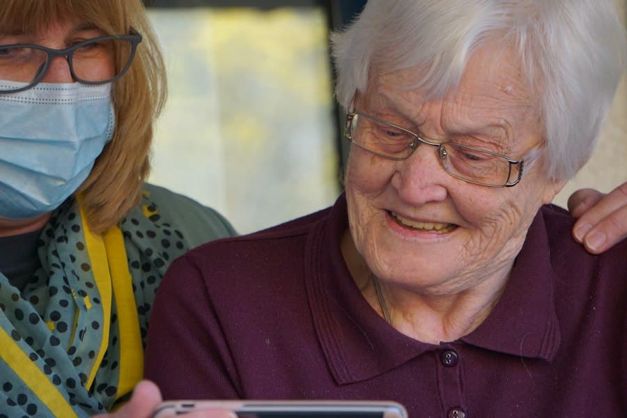 An older woman smiling while a carer shows her a tablet